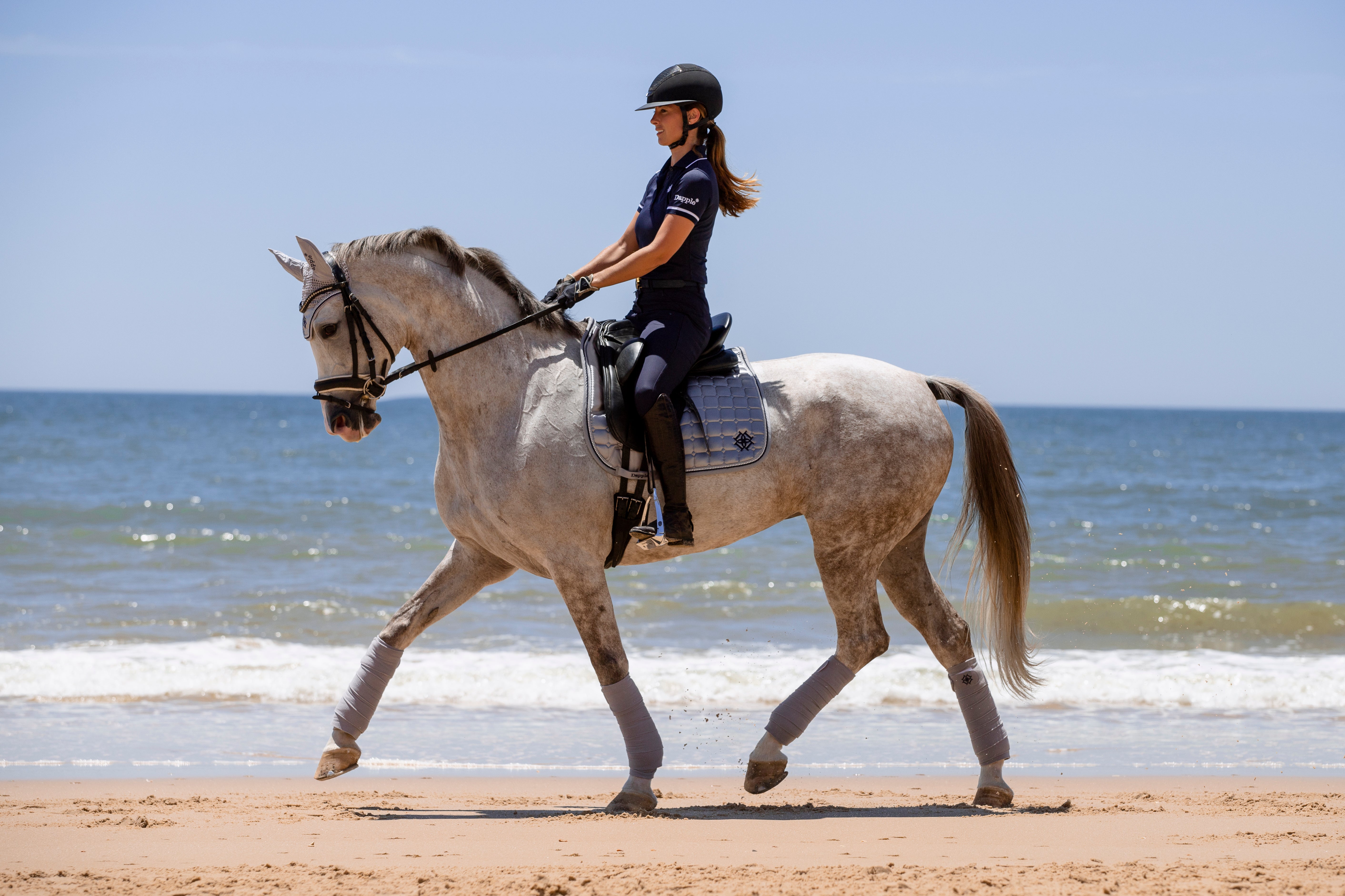 Dressage rider on a beach in Spain riding a White Horse wearing Dapple Equestrian Arctic Silver Dressage Saddle Pad