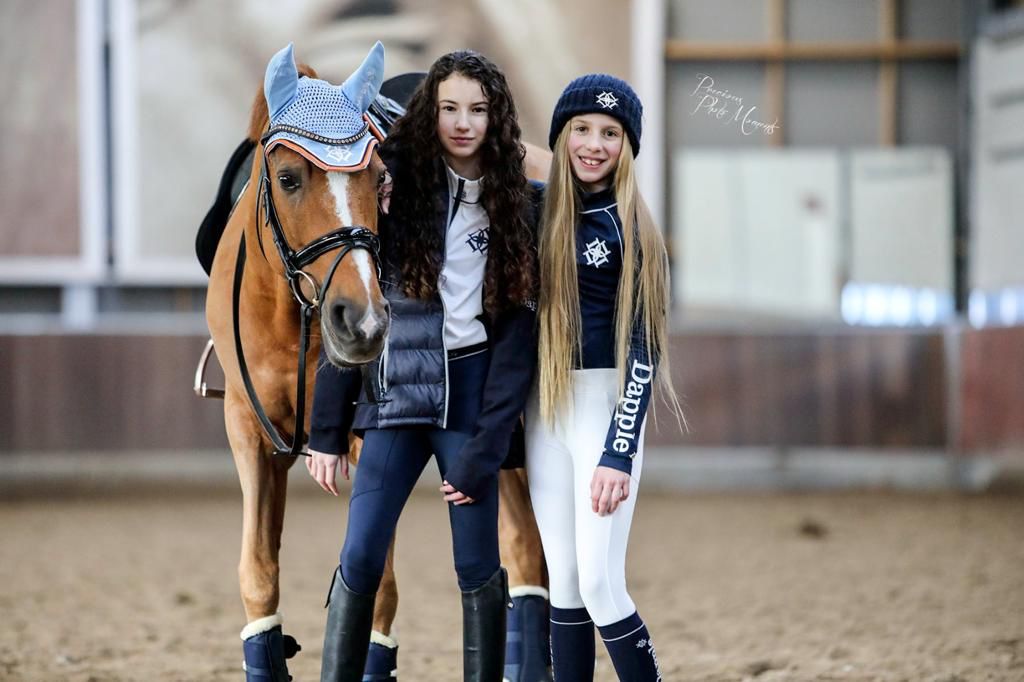 FEI Pony Rider Dina Van Persie with pony rider Soleil Bravenboer both wearing Dapple Equestrian standing beside pony wearing Skey Blue Ear boonet