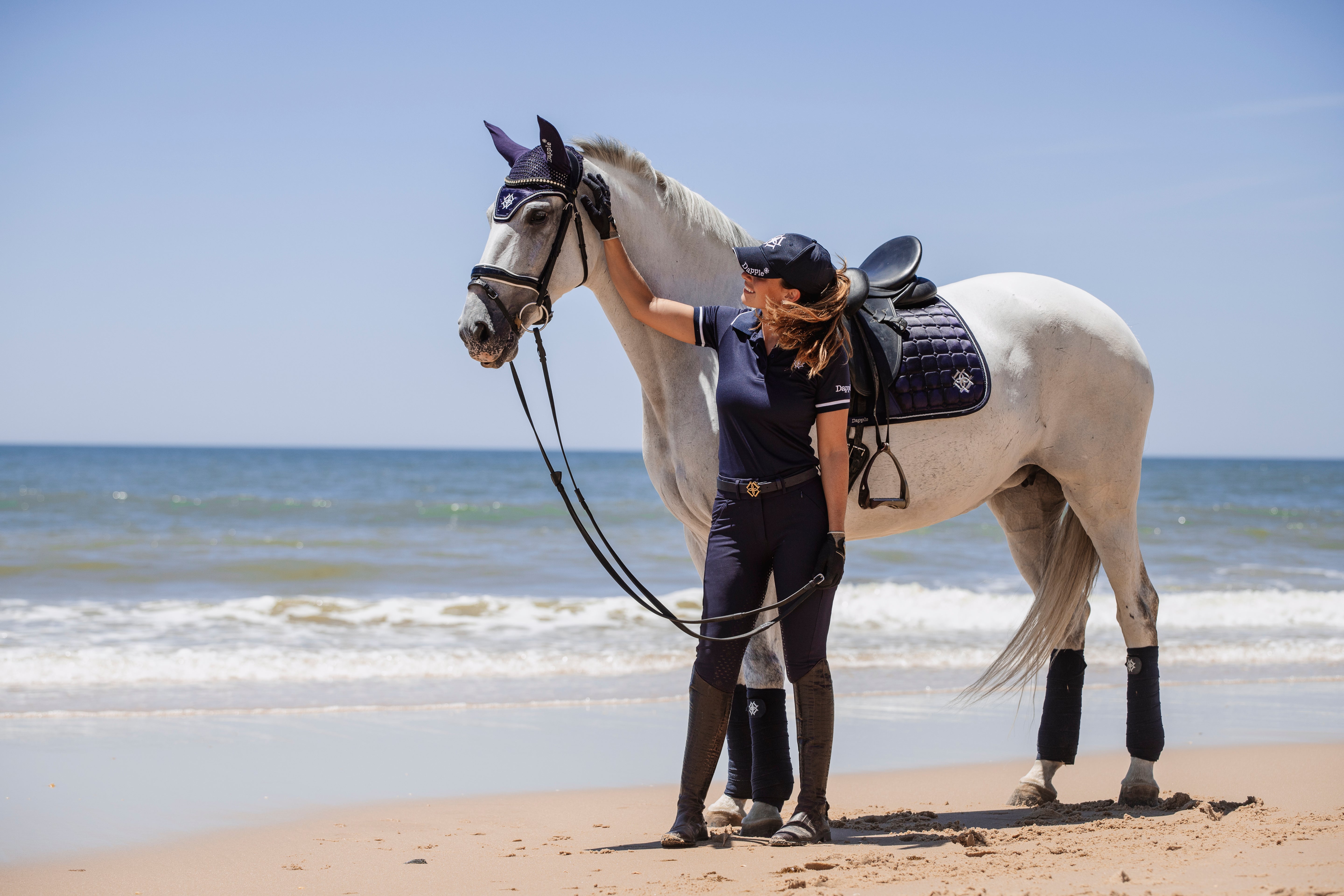 Dressage rider on a beach in Spain with a White Horse wearing Dapple Equestrian Oxford Blue Dressage Saddle Pad