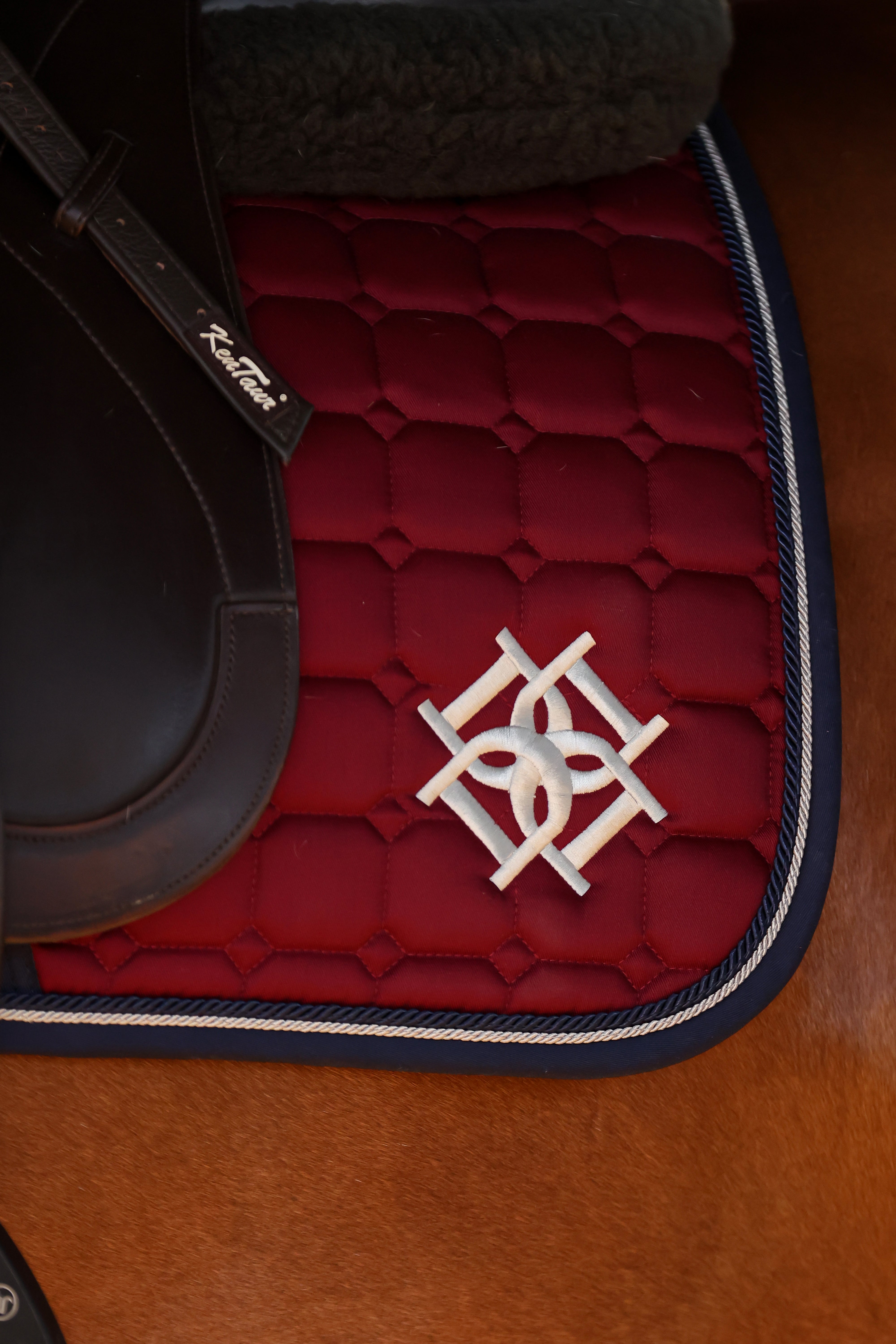 Close up of Dapple Equestrian signature Logo on a Burgundy Saddle Pad with Navy piping and trim